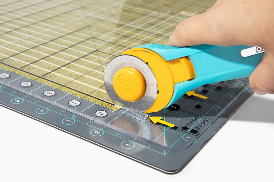Cutting a fabric strip through the slits of a Stripology XL ruler with a rotary cutter