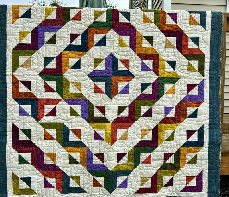 A finished quilt in jewel-tone strips, quilted and bound
